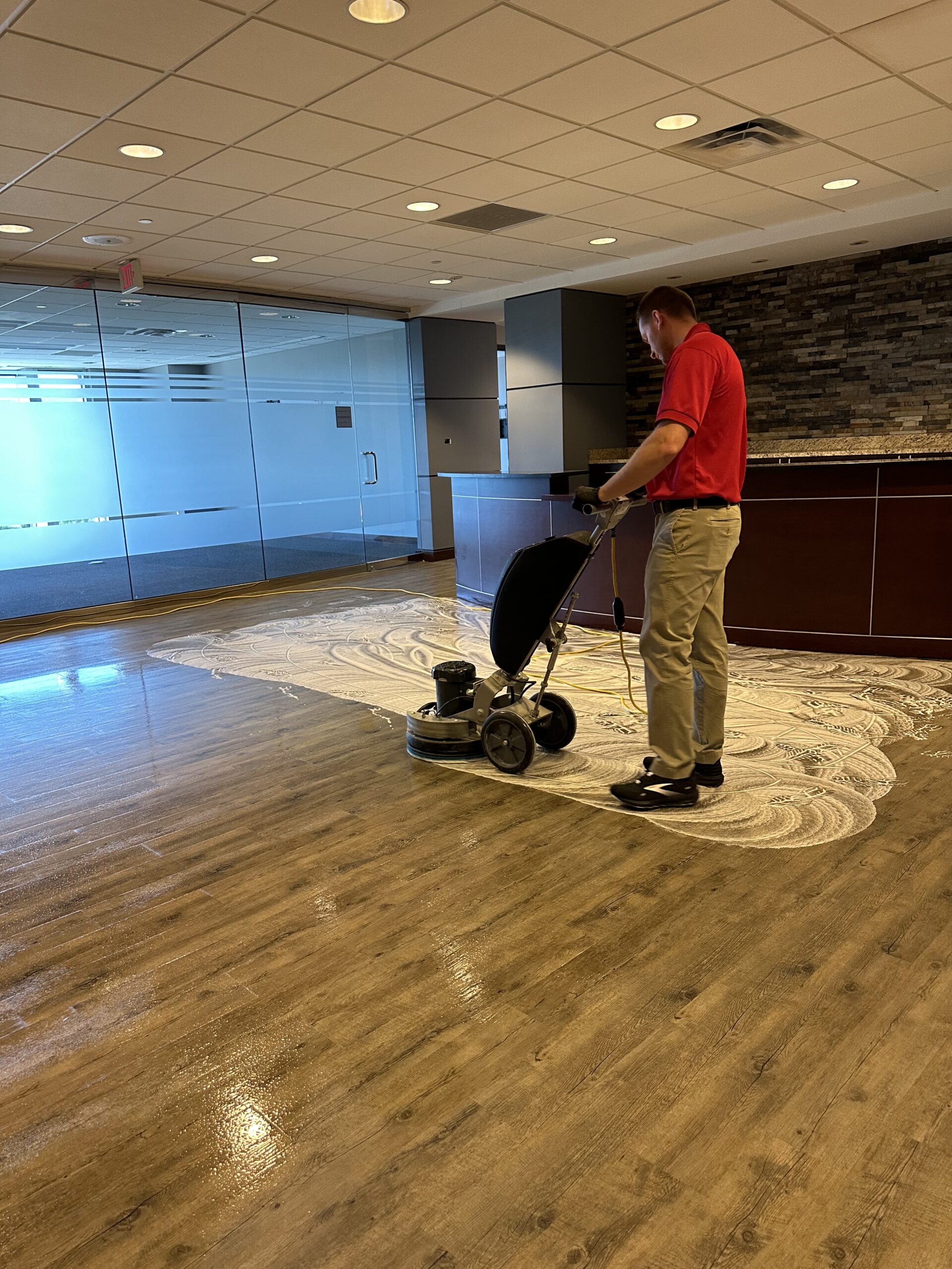 A man in a commercial office room cleaning the floor with a machine. Services by DPM Surface Care