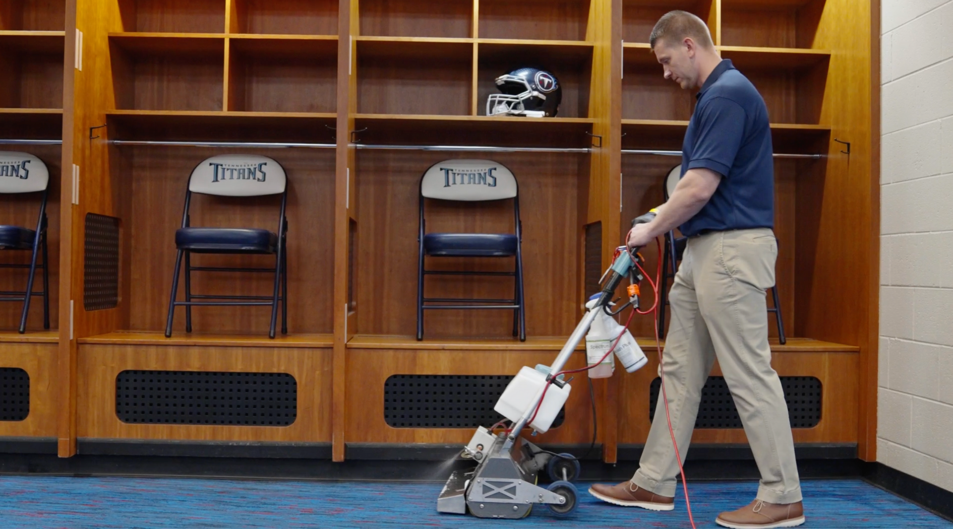 A man inside Titan's locker room, cleaning the carpet with a vacuum. DPM Surface Care