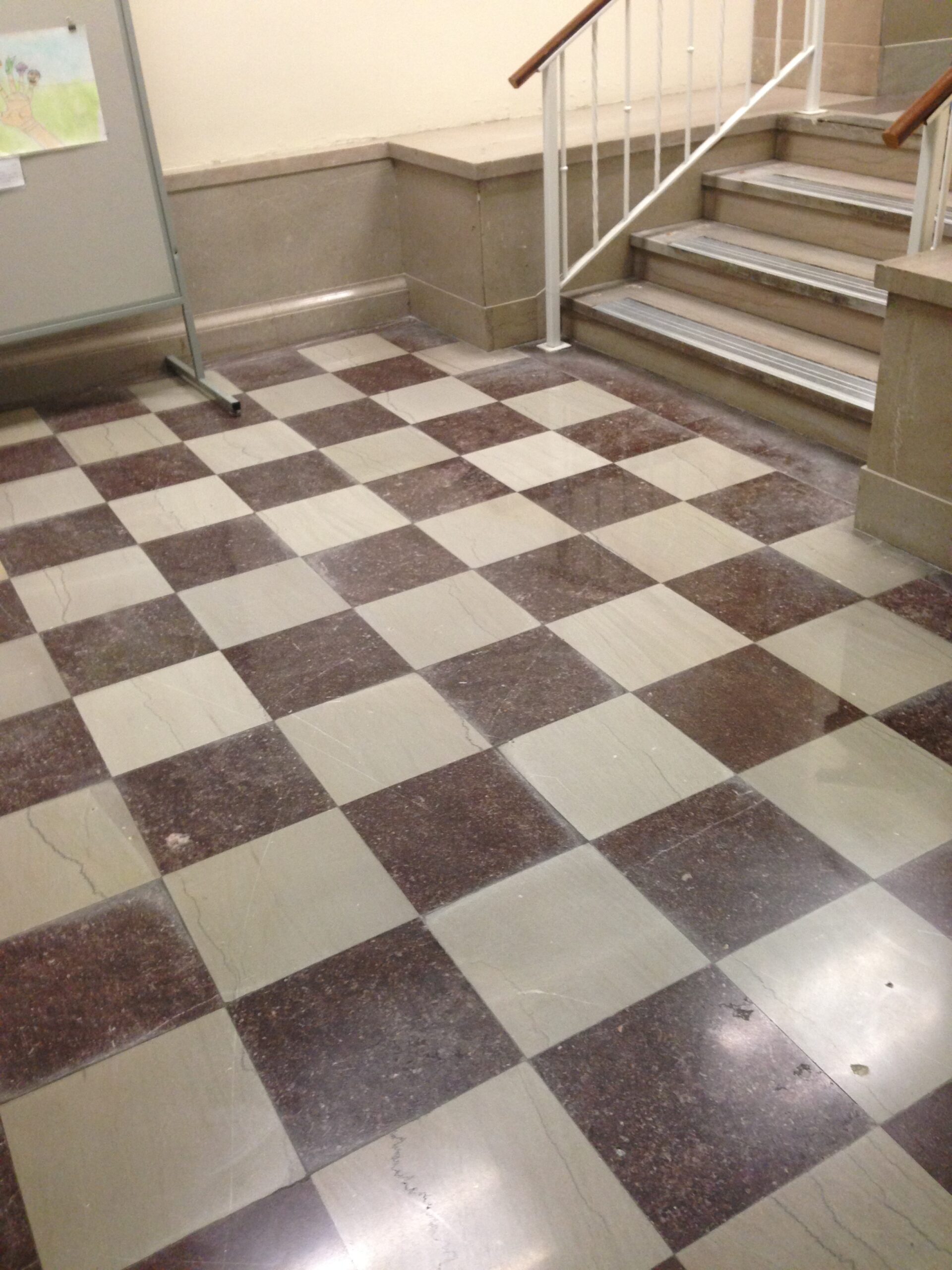 aj building_before A dusty and worn, tiled natural stone floor with a checkered pattern, before cleaning. DPM Surface Care